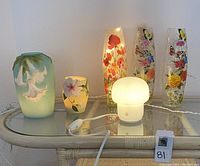 Six decorative lamps displayed on glass table, showing porcelain and floral glass types lit and unlit.