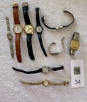 All nine watches laid out on a white/dark cream textured surface showing face and bands