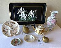 Photo showing a small collection of Asian inspired decorative collectibles including a black iris flower hand-painted tray with cream handles, pink floral ceramic vase, floral-patterned divided treat dish, gold floral teapot, shell-shaped dish with Asian characters, and two small gold bird figurines