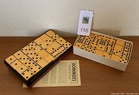 Two sets of Bakelite dominoes, one in a black case and one in a white cardboard tray, with the domino instruction paper underneath.