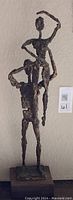 Photo showing the full height of the brutalist bronzed finish dancer sculpture featuring two stylized figures in a stacked dance pose on a wooden base.