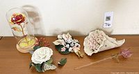 Five floral figurines and one foil rose collectible displayed together on a table