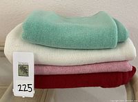 Four folded cashmere ponchos stacked in pink, off white, light green, and deep red colors, showing thickness and texture.