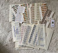 Multiple sheets of postage stamps laid out on carpet, including sleeves with stamps showing various themes and denominations.