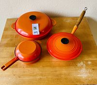 Overview of three items: shallow casserole with lid at top, saucepan with lid bottom left, skillet with wooden handle bottom right.
