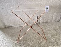 Full view of lucite tray table on carpet showing rose gold metal base and removable lucite tray with handles