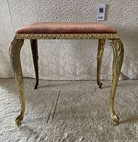 Front view of the gilt metal stool with pink velvet upholstered seat, showing ornate legs and frame.