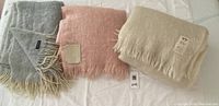 Three mohair blankets laid out: gray with fringe, pink 100% mohair, and cream mohair-wool blend with fringe.