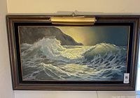 Full view of the framed ocean waves painting with attached brass art light above.