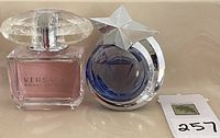 Photo of two perfume bottles: Versace Bright Crystal with pink liquid and Thierry Mugler Angel bottle with blue liquid and silver star cap placed together on a surface