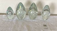 Four Robert Eickholt handblown art glass paperweights in teardrop shapes, arranged from smallest to largest on white towel against white wall.