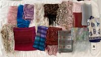Overview of 16 scarves laid out on a white surface, showcasing colors, patterns, and styles