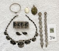 Sterling silver jewelry laid out on white fabric showing bracelets, earrings, pendants with Asian designs and marks.