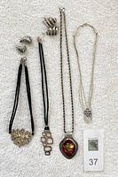 Full view of all jewelry pieces including cylinder bead necklace, cord necklaces with pendants, and four pairs of silver earrings.