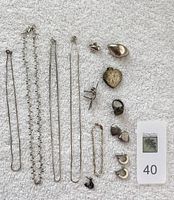 Full lot of sterling silver jewelry displayed on white towel including chains, pins, rings, bracelets, and earrings.
