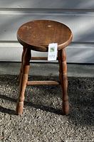 Photo of a round wooden stool with three legs and cross braces showing wear on the ground in natural light.
