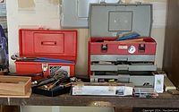 Two toolboxes on a wooden surface holding assorted hand tools including hammers, screwdrivers, and other tools