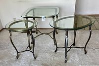 Trio of glass tables: round, oblong, and square shaped with metal legs, displayed on carpeted floor.