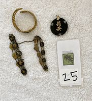 Photo showing two Siam bracelets (black and gold-tone Asian motifs), carved black pendant with gold characters, and 1939 Golden Gate Exposition bracelet