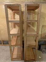 Two wooden shelving units side by side in a basement setting, showing front view of five shelves each.