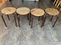 Four stools shown from the front with round wood tops and metal legs arranged in a row.