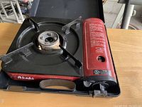 Red Akahi portable gas cooker closed, showing burner top and control knob.