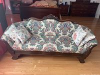 Full front view of the antique mahogany sofa showing floral upholstery and wooden frame detailing.