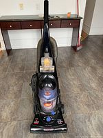 Front view of black Bissell upright vacuum cleaner showing controls and dust canister