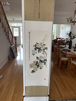 Vertical full view of the scroll hanging showing the full chrysanthemum painting and scroll borders in a living room setting.
