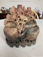 Front view showing three vases with floral and leaf carvings with a carved stone base in natural soapstone colors.
