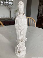 Front view of white porcelain goddess statue showing face, robes, and detailed base with floral motifs.