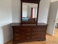 Full front view of the solid wood dresser with attached mirror showing all drawers and reflective surface.
