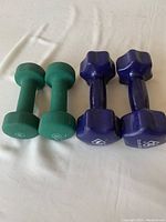 Two pairs of dumbbells laying side by side on a white surface: green 5 lb and purple 9 lb.