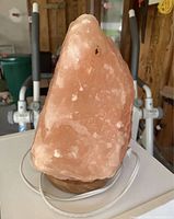 Front view of large raw pink salt lamp on round wooden base with white electrical cord and switch visible.