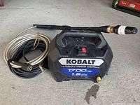 Overall image of Kobalt electric pressure washer unit with attached spray wand and two hoses coiled beside it.