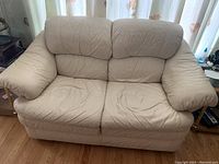 Close-up of the white leather loveseat showing cushioned back rest and armrests with visible usage creases