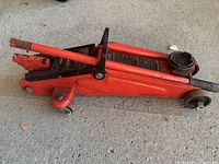Side view of red Motocraft hydraulic trolley jack showing full length and handle attached