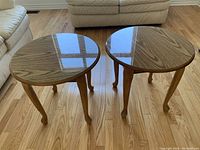 Pair of round wooden coffee tables with glass tops, placed side by side on hardwood floor showing the front view.