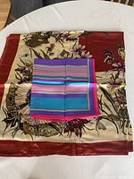 Two silk scarves laid flat on a table: one large floral print scarf and one smaller striped scarf.