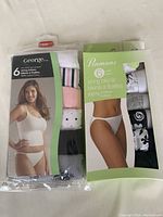 Front image of two sealed bags containing 6-packs of small size string bikini underwear from George and Penmans brands, showing model images and variety of colors in packaging.