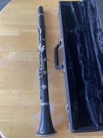 Student clarinet placed on a wooden table next to the open hard case, showing the main clarinet body laid flat.