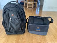 Front view of black carry-on backpack and black soft satchel bag on wooden floor