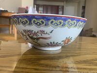 Side view of the bowl showing detailed hand-painted bird and flower designs with yellow and blue decorative band near the rim.