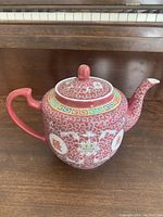 Full side view of the pink famille rose teapot showing detailed floral and geometric patterns, longevity symbols, curved spout and handle.