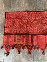 Photo showing detailed section of red embroidery floral and vine patterns with mirror embellishments and panel tassels