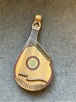 Miniature Ukrainian bandura on carpeted floor, 12+ metal strings, decorative rosette
