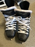 Front view of black Bauer hockey skates with white laces tied, showing cushioned interior padding and skate blades.