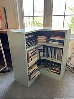 Front view of the corner shelf filled with books showing three shelves and storage space.