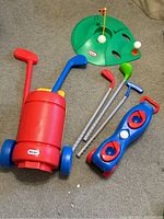 Photo of red and blue plastic golf caddies, four plastic golf clubs, and green putting green with balls and tee.