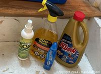 Six bottles of cleaning supplies including OdoBan, Goo Gone, Drano, Krud Kutter, and Clorox sprays and cleaners shown on wooden stairs.